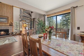 A dining area with a fireplace, a spiral staircase, and a large window with a view of trees. - Tahoe Tyrol Chalet - Two Bedroom House, Sleeps 4 (South Lake Tahoe)