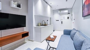 Ein modernes Wohnzimmer mit Flachbildfernseher, grauem Sofa und einem kleinen Tisch.