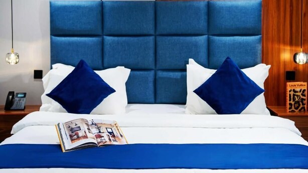 Ein Hotelzimmer mit einem großen Bett, einem blauen Kopfteil, weißer Bettwäsche und einer Zeitschrift auf dem Bett.