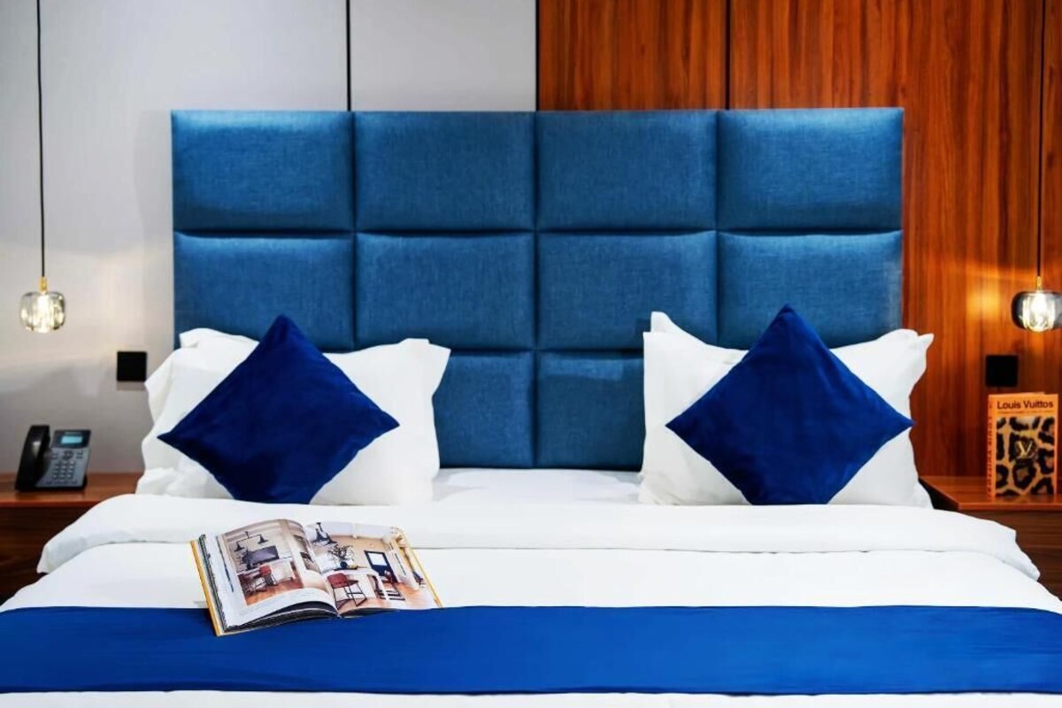 Ein Hotelzimmer mit einem großen Bett, einem blauen Kopfteil, weißer Bettwäsche und einer Zeitschrift auf dem Bett.