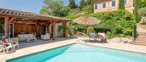 Une piscine avec des chaises longues et un espace de détente abrité.