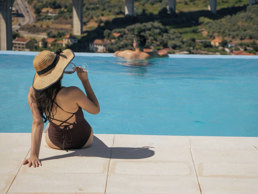 Eine Person sitzt am Pool mit Blick auf eine Brücke und viel Grün im Hintergrund.