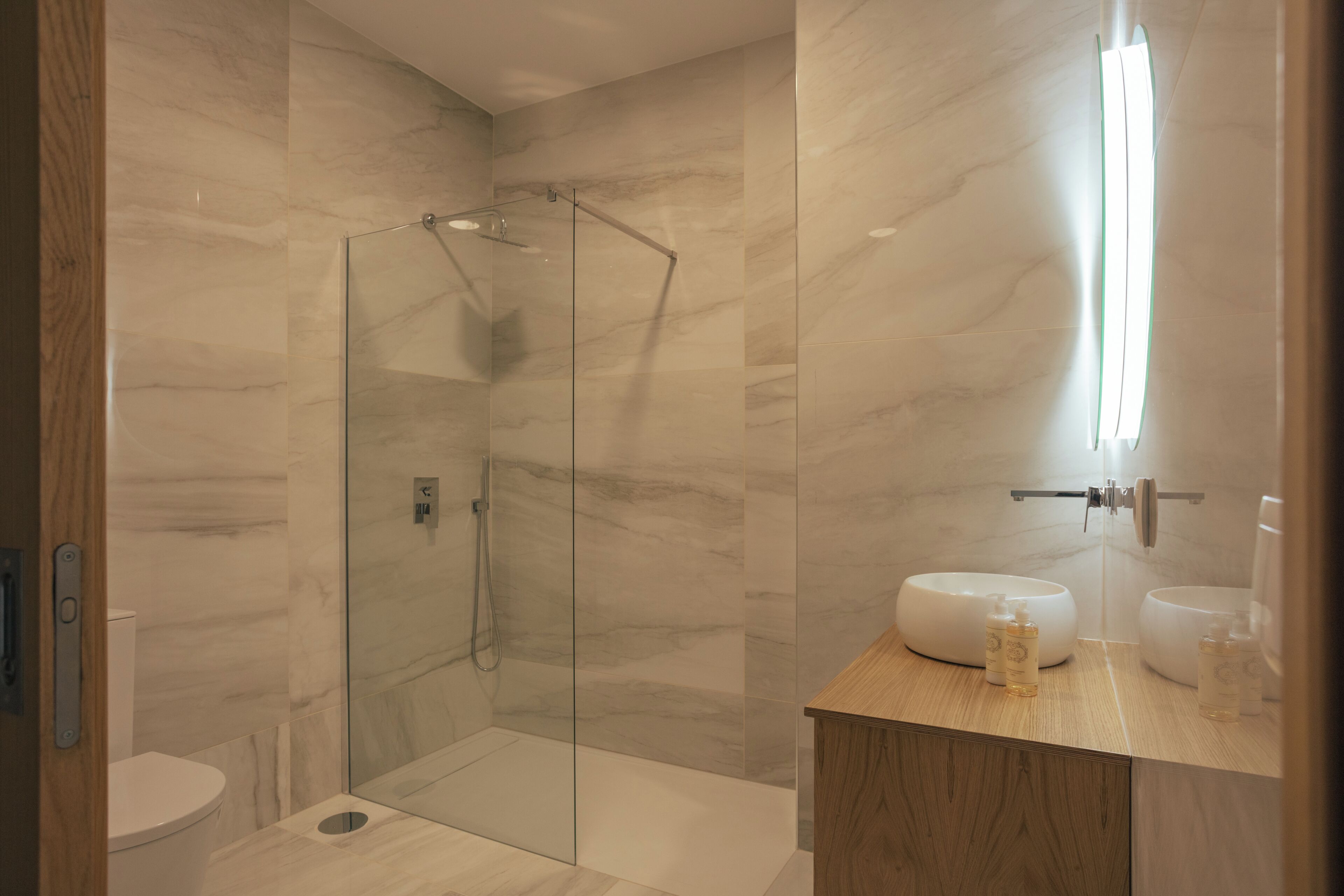 A modern bathroom with a glass-enclosed shower, a wooden vanity, and a marble wall.
