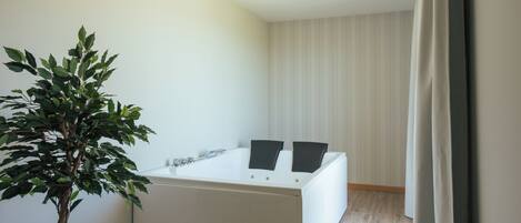 A modern bathroom with a bathtub, a potted plant, and a striped wall.