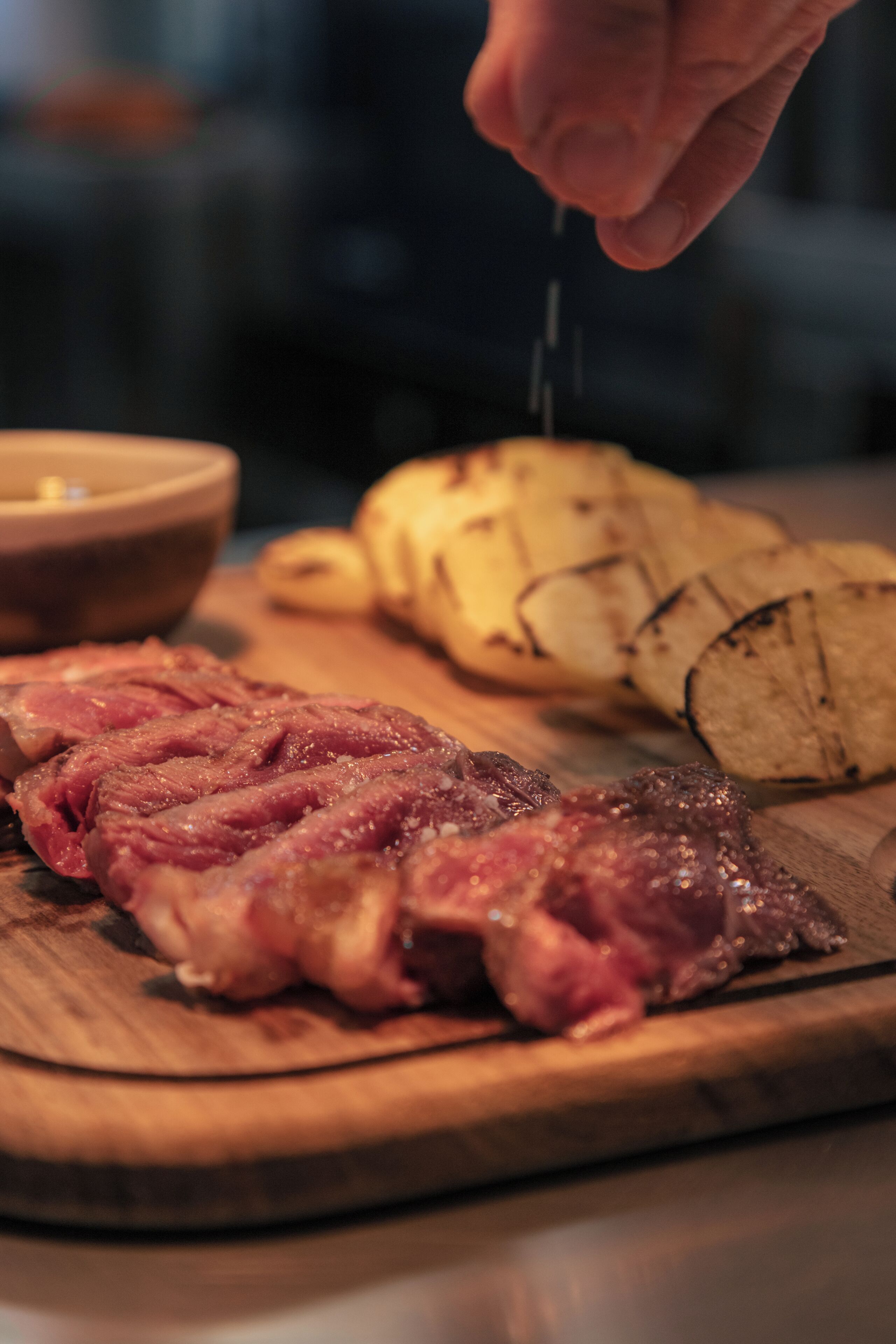 Ein Holzschneidebrett mit einem Steak und Kartoffelscheiben.