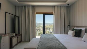 Una habitación de hotel con cama, televisión, balcón con vistas y ventana con cortinas.