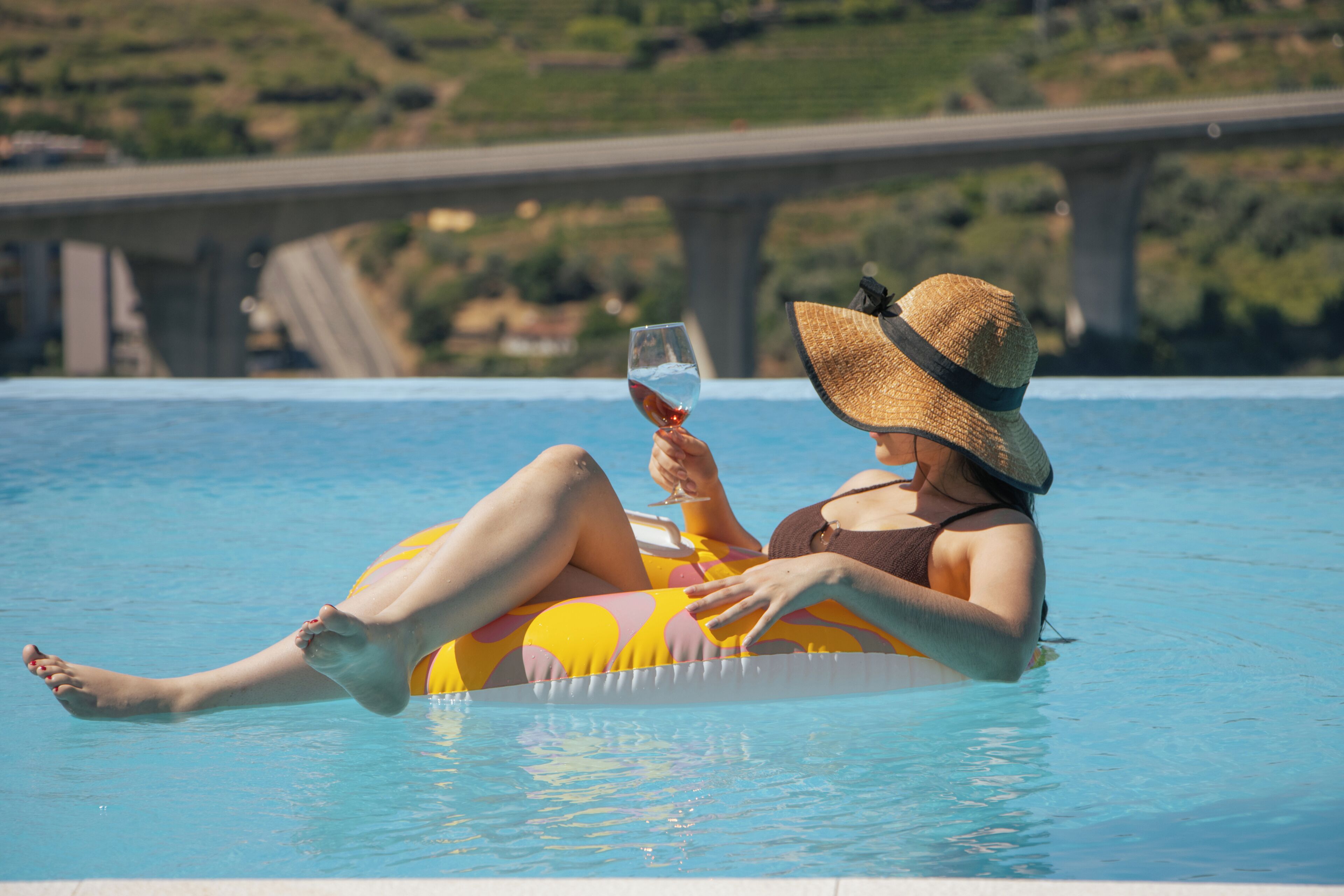 A person relaxing on a pool float in a swimming pool with a bridge in the background.