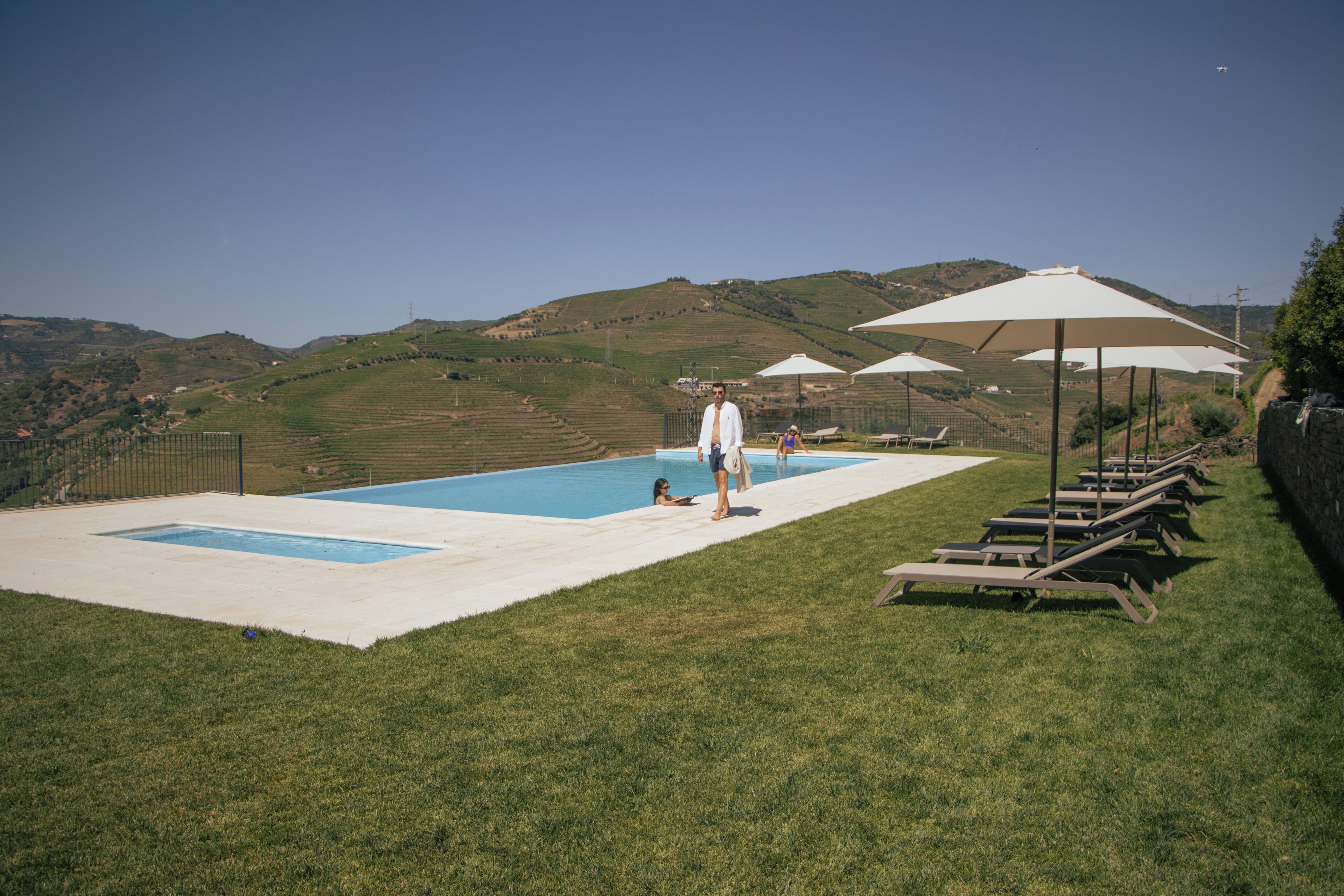 Une piscine divisée en deux zones contiguës, entourée d’une pelouse agrémentée de chaises longues et de parasols.