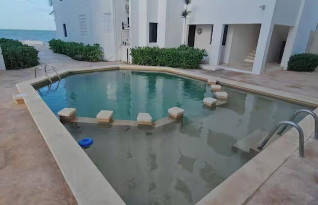 A swimming pool with steps leading into it, surrounded by a building with a view of the sea.