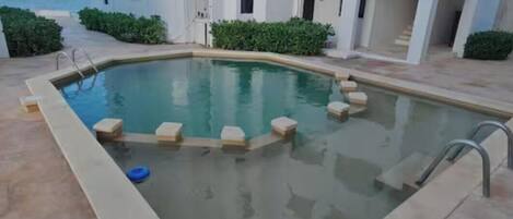 A swimming pool with steps leading into it, surrounded by a building with a view of the sea.