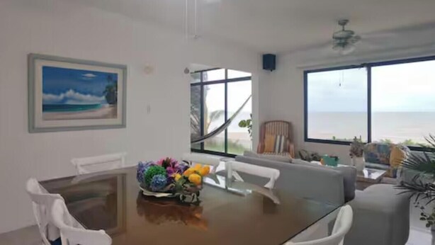 A dining area with a table, chairs, a painting, and a view of the ocean. - Beachfront Apartment | Ground Floor and Pool (Progreso)