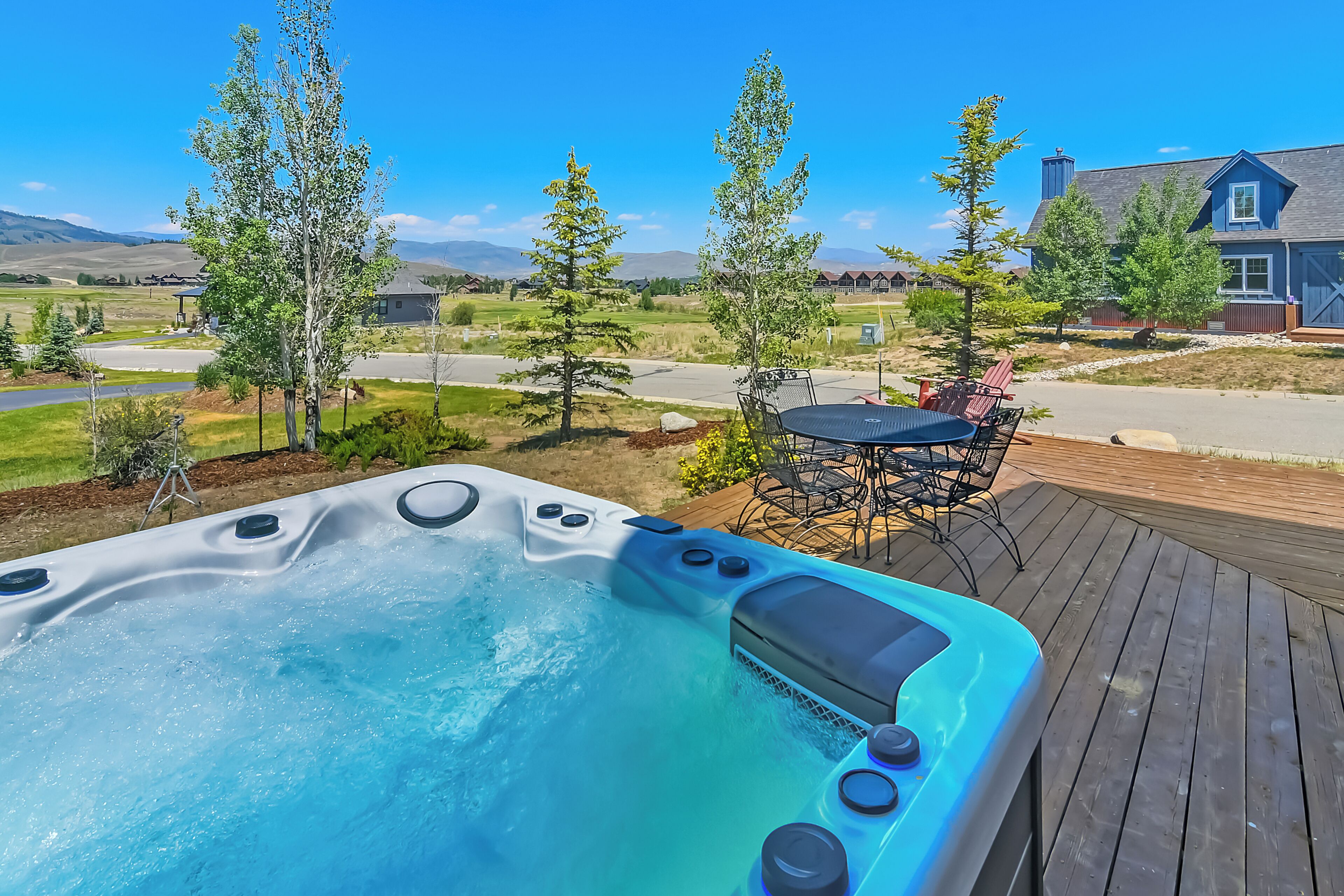 Een hottub op een houten terras met uitzicht op een woonwijk en bergen.