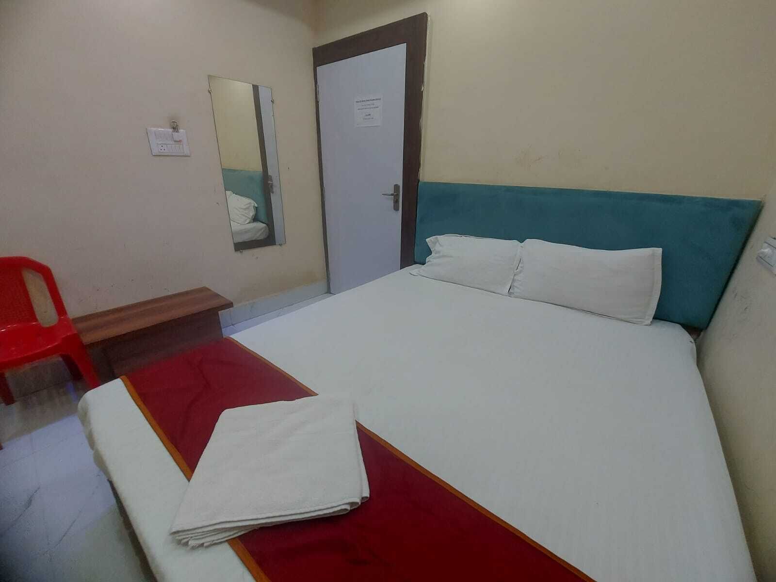 A hotel room with a bed, a red chair, a small table, and a door with a mirror.