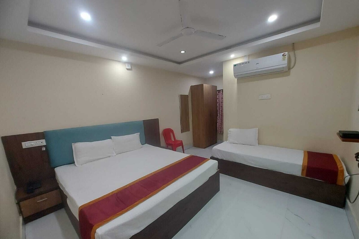Quarto de hotel com duas camas, um ventilador de teto, aparelho de ar condicionado e uma cadeira vermelha.