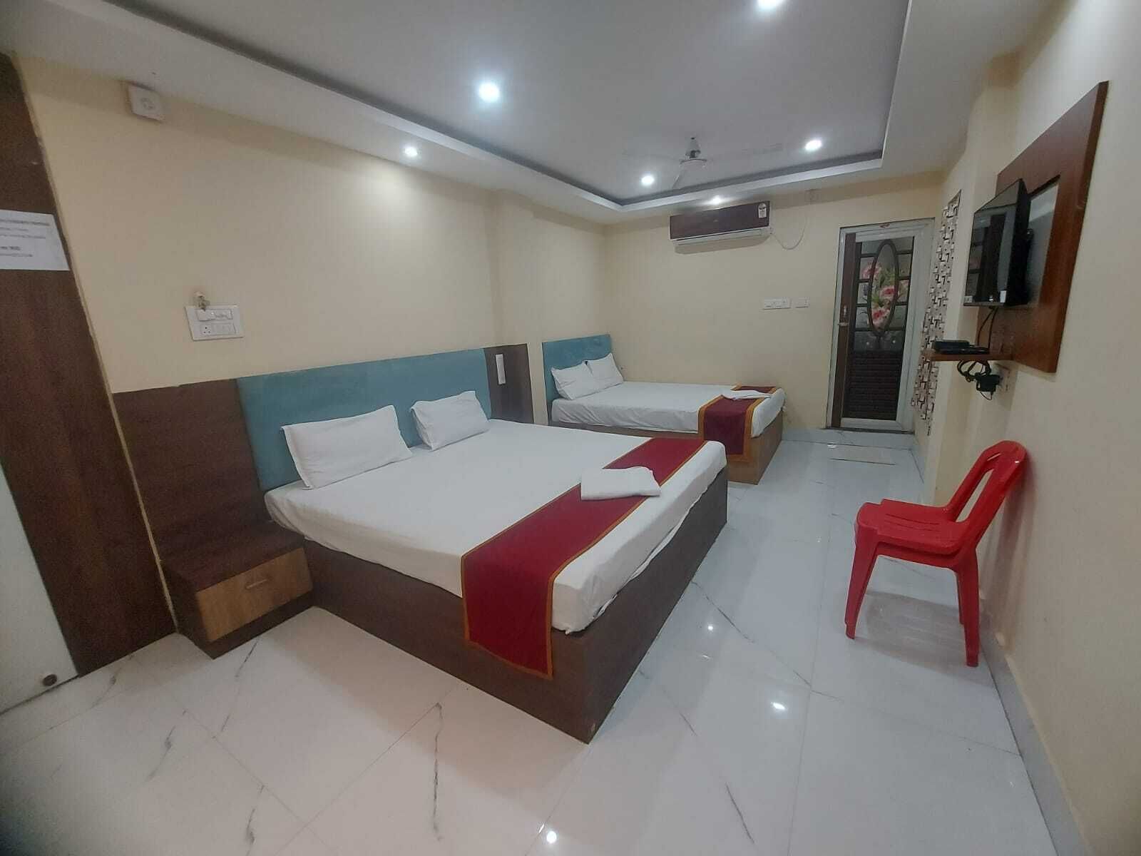 A hotel room with two beds, a red chair, a TV, and an air conditioning unit.