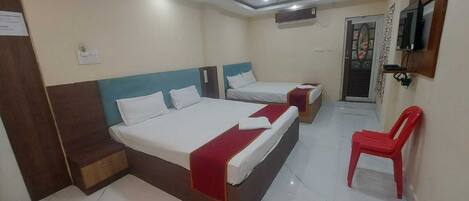 A hotel room with two beds, a red chair, a TV, and an air conditioning unit.