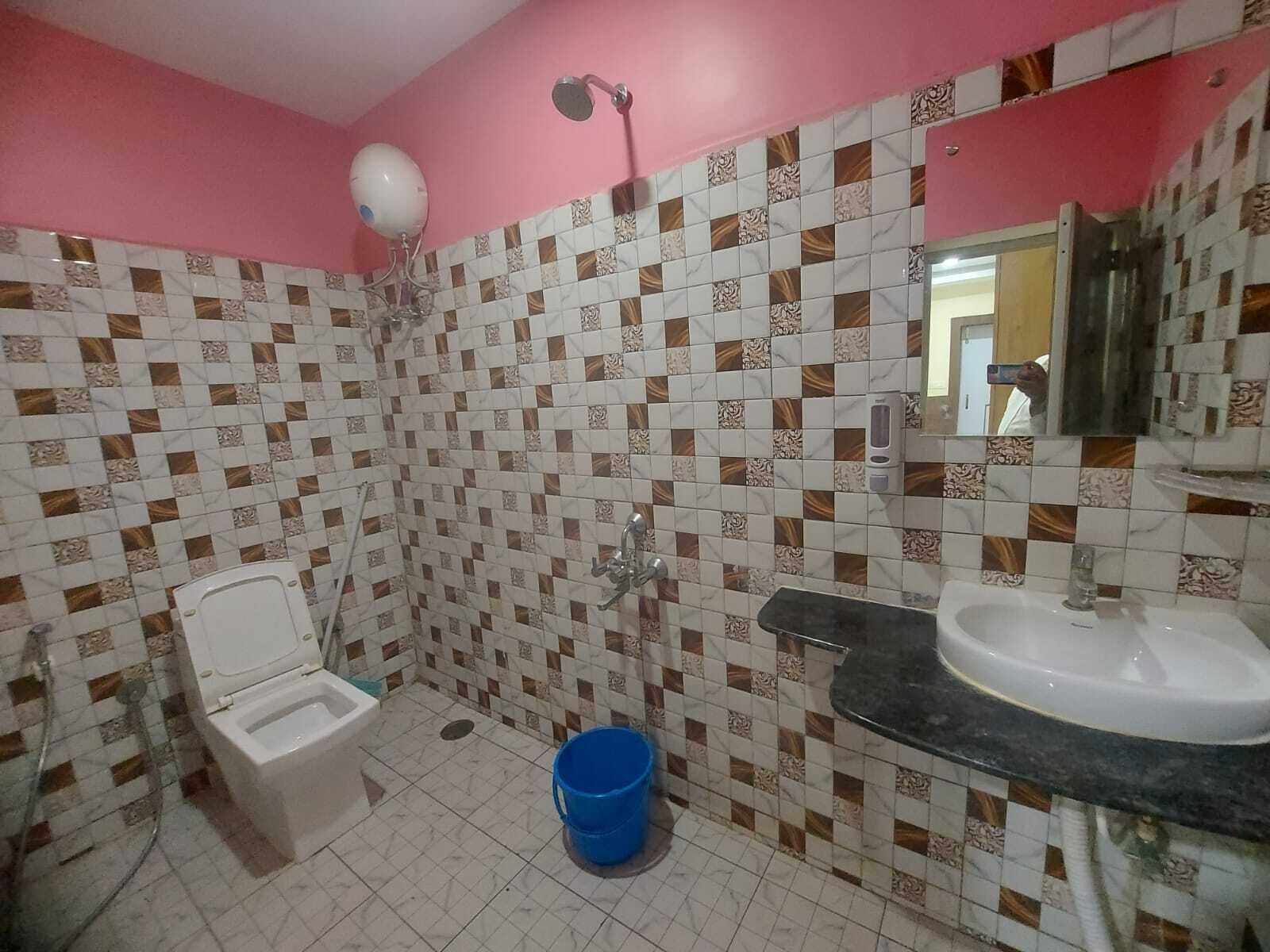 A bathroom with a toilet, shower, sink, and a blue bucket on the floor.