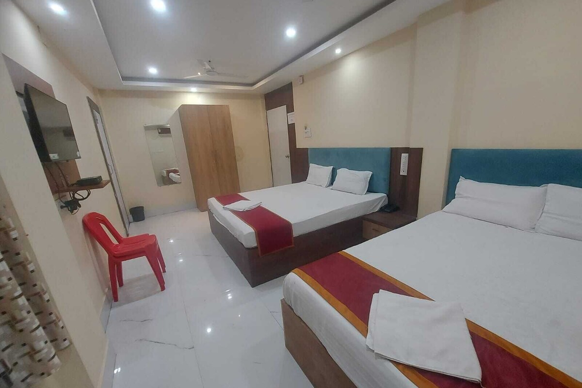 Quarto de hotel com duas camas, uma cadeira vermelha, um guarda-roupa e um espelho.
