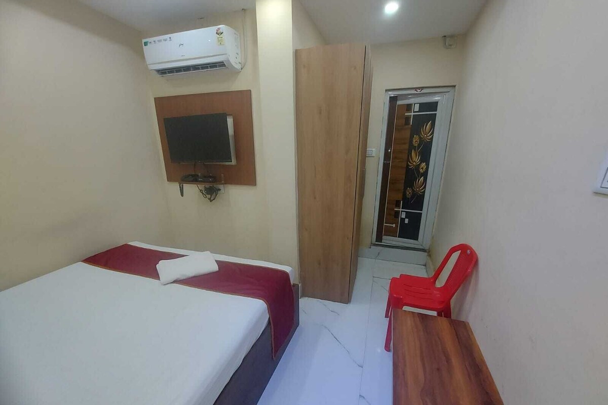 Quarto de hotel com cama, televisão na parede, ar condicionado, guarda-roupa de madeira e uma cadeira vermelha.