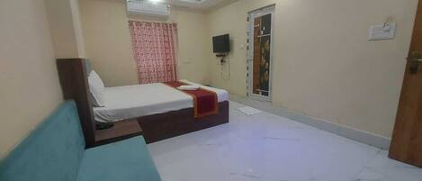 A bedroom with a bed, a blue sofa, a TV, and an air conditioning unit.