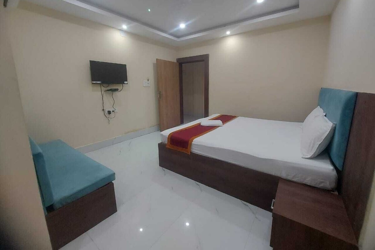 Quarto de hotel com cama, televisão, guarda-roupa e um pequeno espaço de estar.