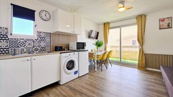A compact kitchen with a washing machine, a microwave, and a dining area with yellow chairs.