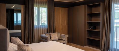 A modern bedroom with a large bed, a seating area, built-in shelving, and a large window.