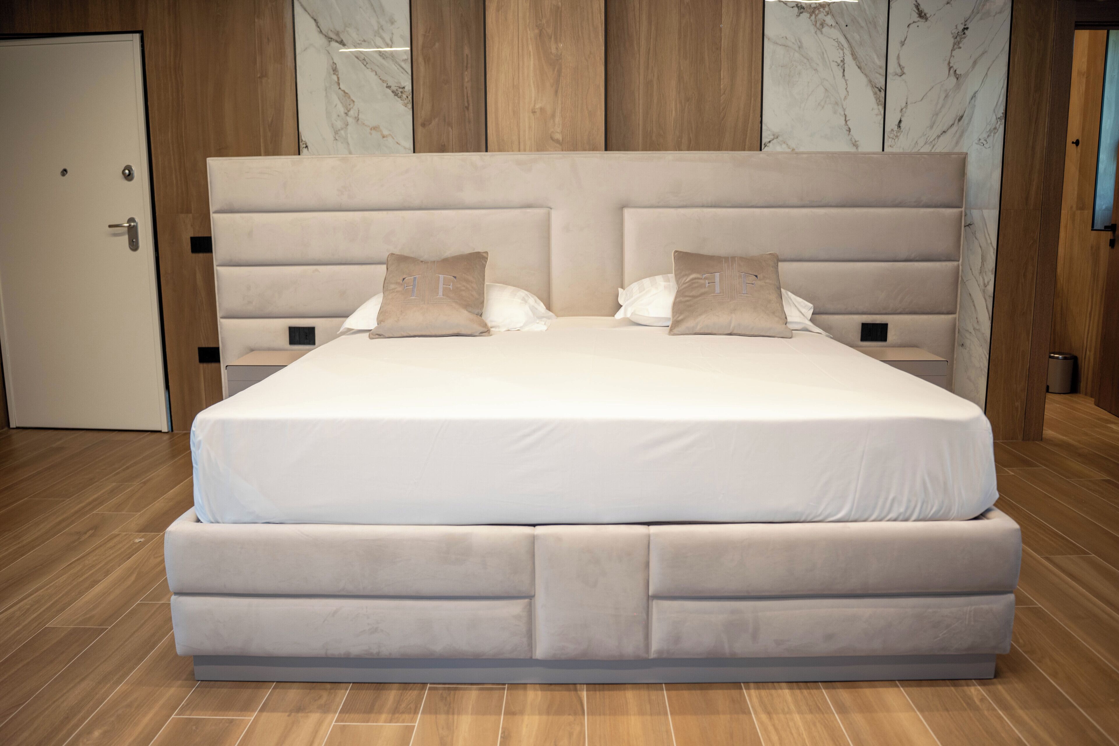 Een tweepersoonsbed met hoofdbord, twee kussens en een houten vloer.