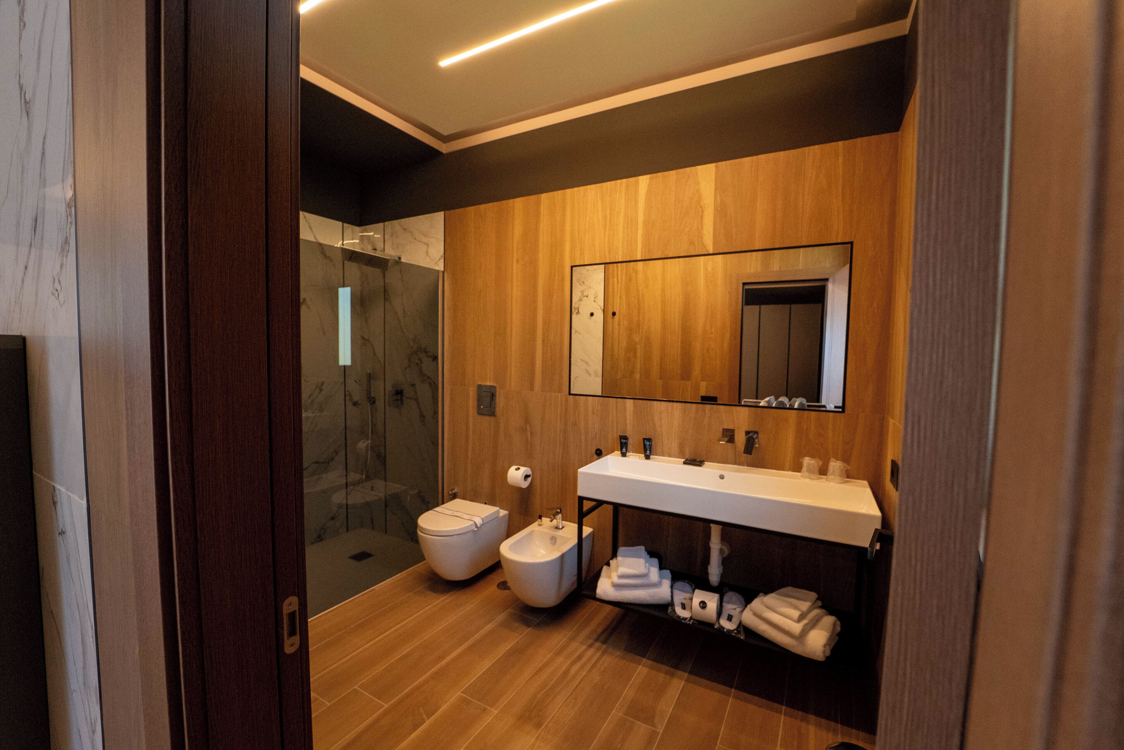 A modern bathroom with a wooden vanity, a glass shower enclosure, and a marble-tiled floor.