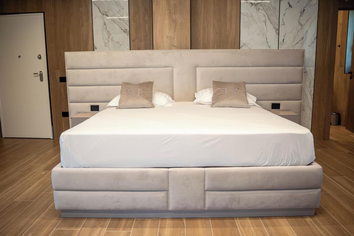 A large bed with a padded headboard, two pillows, and a wooden floor.