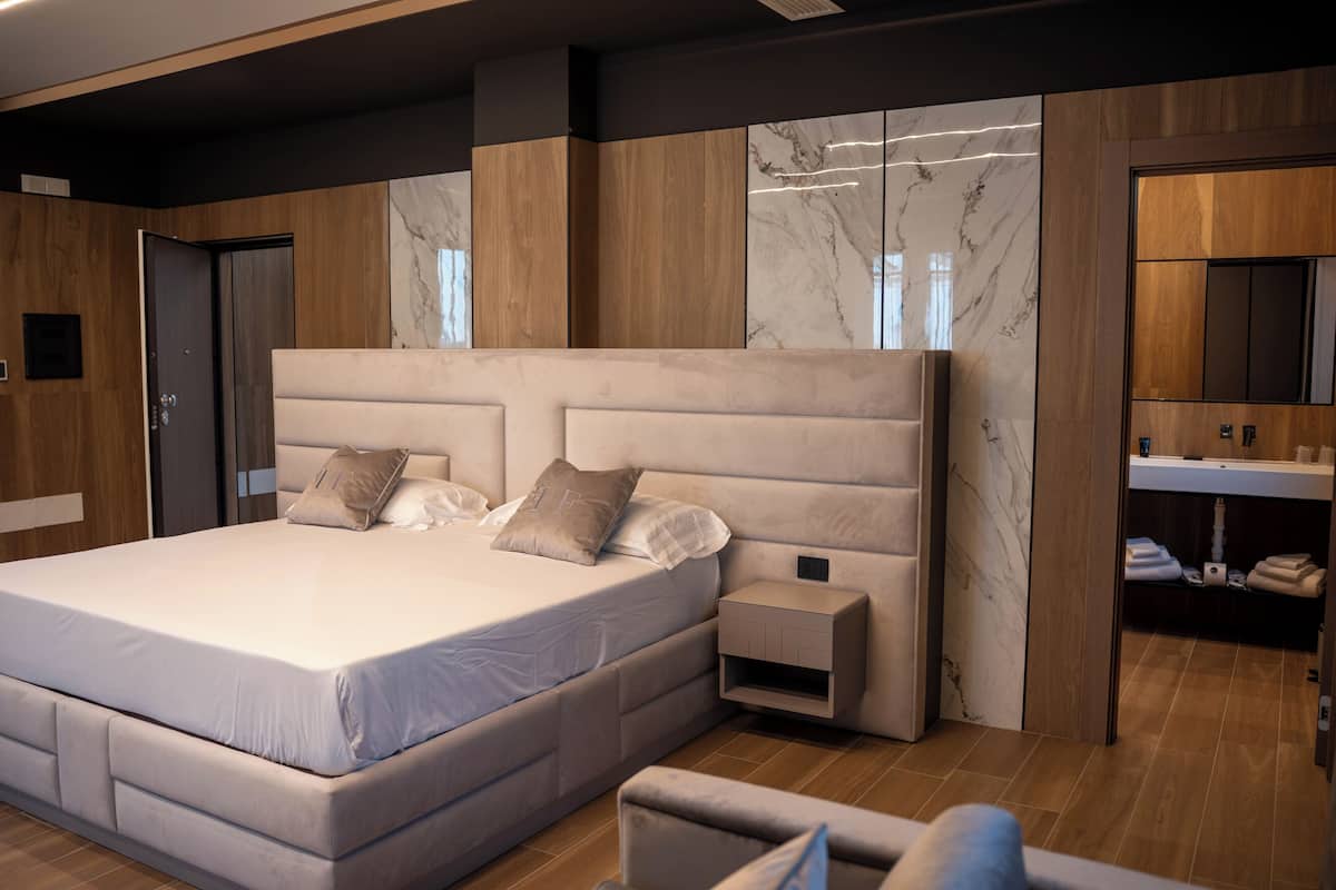 A modern bedroom with a large bed, bedside tables, a built-in wardrobe, and a bathroom with a mirror and sink.