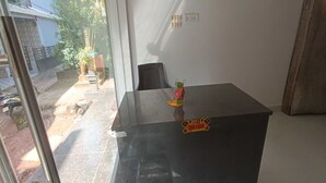 Ein Zimmer mit einem schwarzen Schreibtisch, einem Stuhl, einem kleinen dekorativen Gegenstand auf dem Schreibtisch und einem Fenster mit Blick ins Freie.