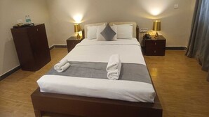 Ein Hotelzimmer mit einem großen Bett, zwei Nachttischen mit Lampen, einem Holzschrank und einem Vorhang.