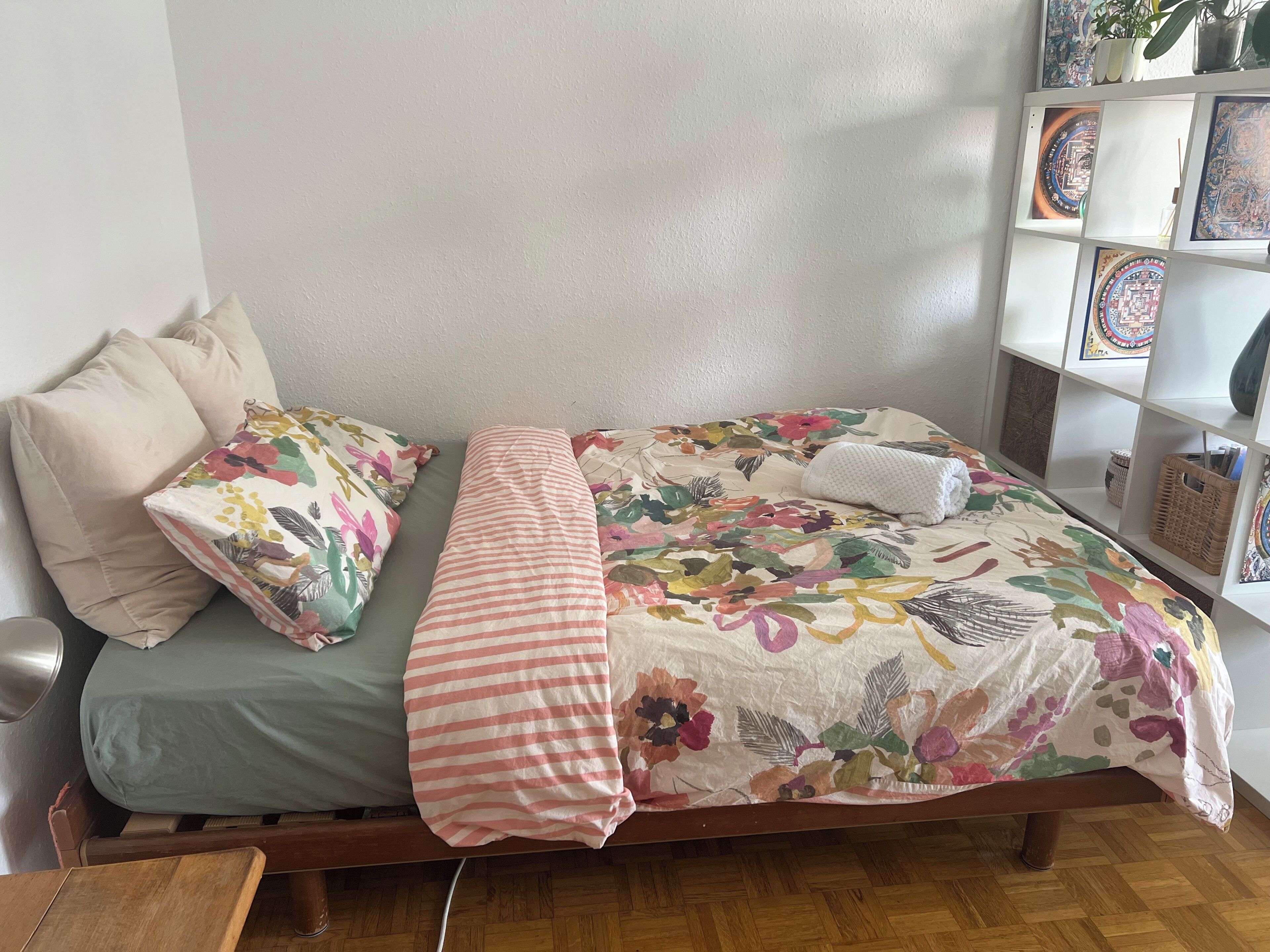 Una cama con ropa de cama floral, una manta a rayas y una almohada.