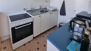 Una cocina con armarios blancos, estufa, fregadero y encimera con un hervidor y una botella.