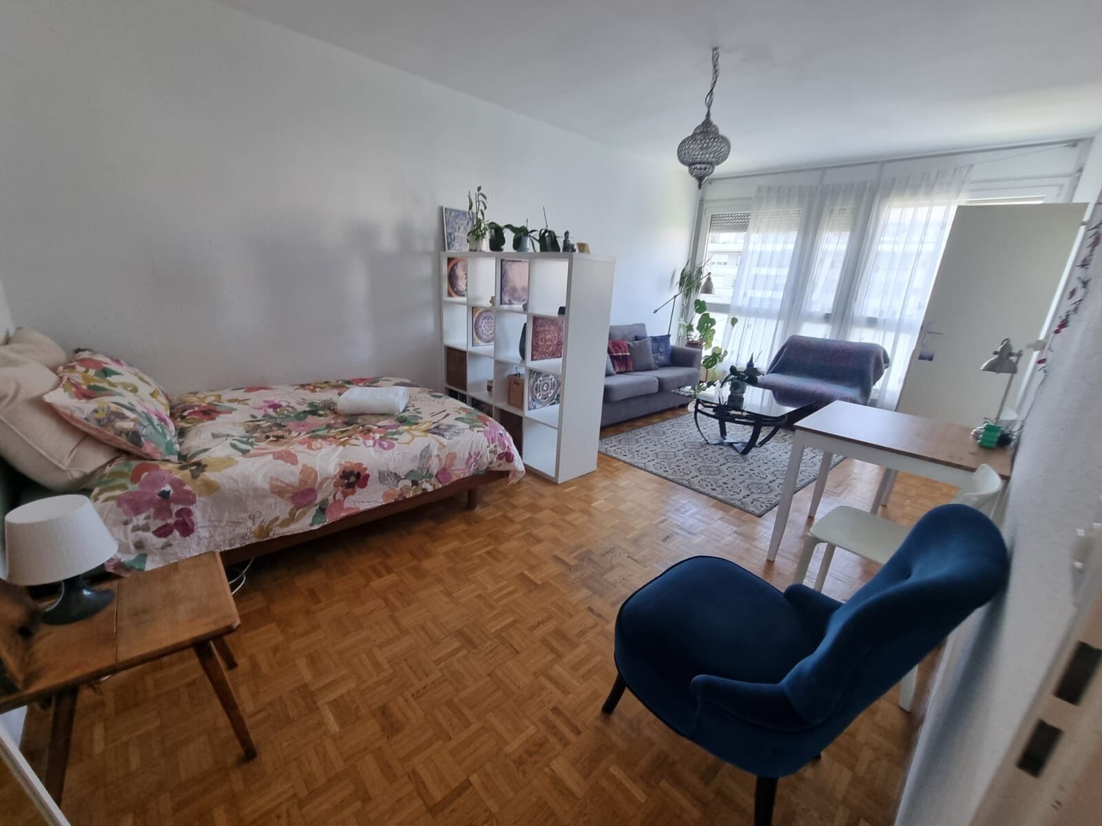A bedroom with a bed, a desk, a chair, a sofa, and a shelving unit.