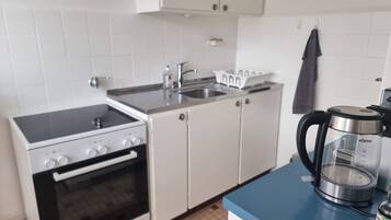 Une cuisine compacte équipée d’une cuisinière, d’un four, d’un évier et d’une machine à café posée sur le plan de travail.