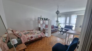 Un espacio habitable pequeño con cama, sofá, mesa de centro, silla y estante con adornos.