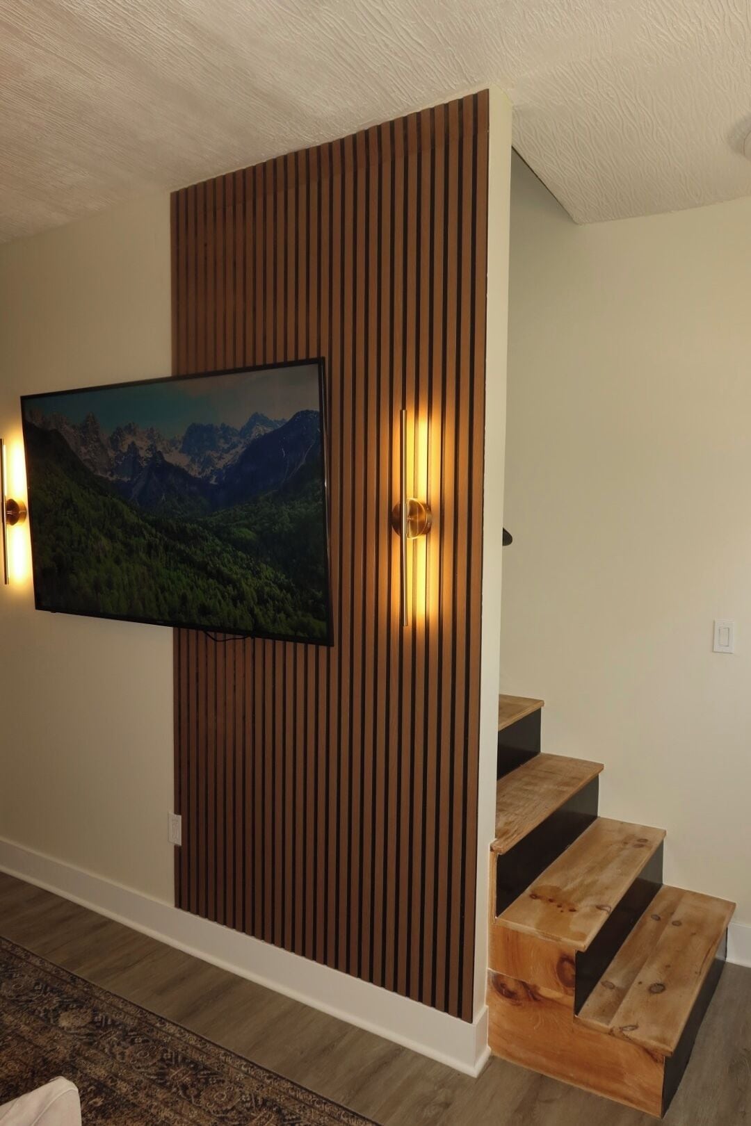 Un interior moderno con un panel de madera, un televisor montado y una escalera.