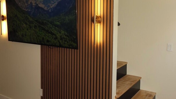 A modern interior with a wooden panel wall, a mounted TV, and a staircase. - LUXURY DOWNTOWN COLUMBUS TOWNHOME (Columbus)