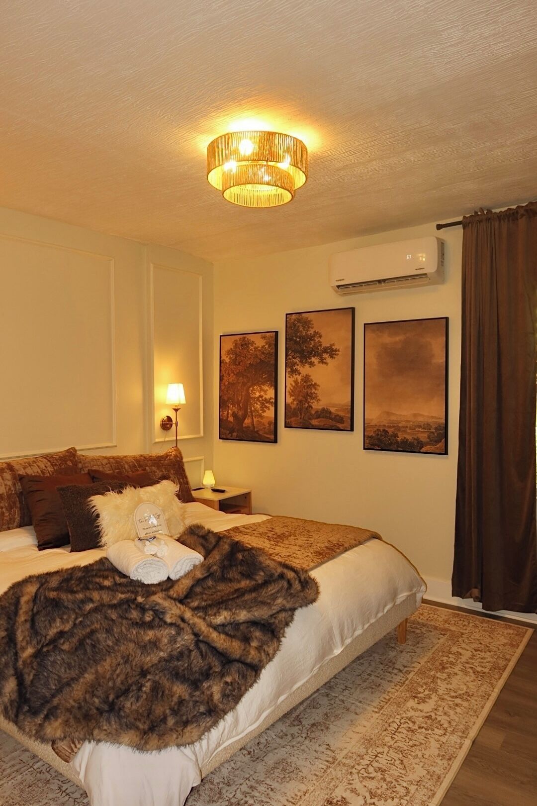 Una habitación de hotel con una cama, una lámpara de araña, aire acondicionado y tres cuadros en la pared.