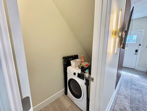 A laundry room with a washing machine, a dryer, and a small shelf with cleaning supplies. - LUXURY DOWNTOWN COLUMBUS TOWNHOME (Columbus)