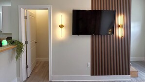 A modern living room with a flat-screen TV mounted on a wall, a wooden panel feature, and a door leading to another room. - LUXURY DOWNTOWN COLUMBUS TOWNHOME (Columbus)