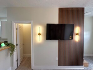 A modern living room with a flat-screen TV mounted on a wall, a wooden panel feature, and a door leading to another room. - LUXURY DOWNTOWN COLUMBUS TOWNHOME (Columbus)