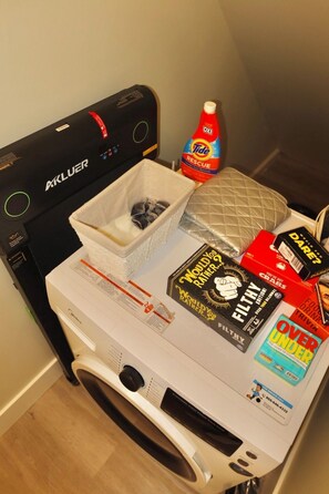A front-loading washing machine with a basket, Tide detergent, a quilted pillow, and a few books. - LUXURY DOWNTOWN COLUMBUS TOWNHOME (Columbus)