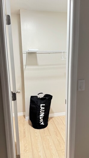 Ein Zimmer mit Holzboden, einer weißen Tür, einer weißen Wand und einem schwarzen Wäschebeutel mit dem Aufdruck 'LAUNDRY'.