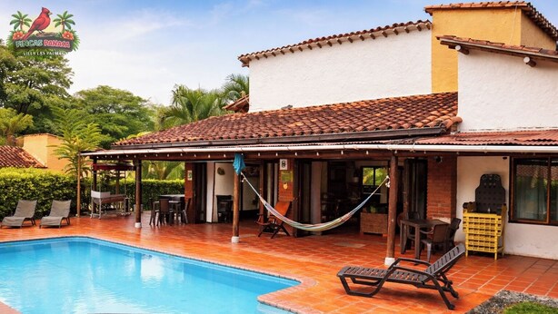 Area piscina con solarium piastrellato, sedie a sdraio, un'amaca e una veranda coperta.
