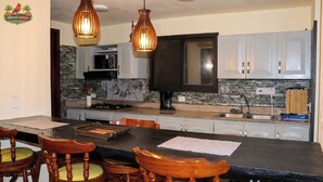 Una cucina con ripiani in granito, un'isola nera, sedie di legno e lampade a sospensione.