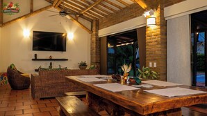 Un'area pranzo con tavolo in legno, mobili in vimini e TV montata a parete.