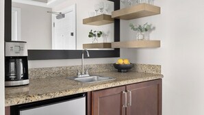 Una cocina con encimeras de granito, un lavamanos de acero inoxidable, repisas de madera sobre la encimera y una cafetera.